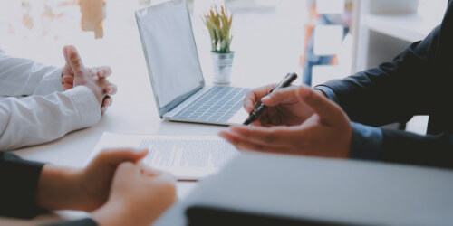 Drei Personen besprechen ein Dokument an einem Tisch mit Laptop